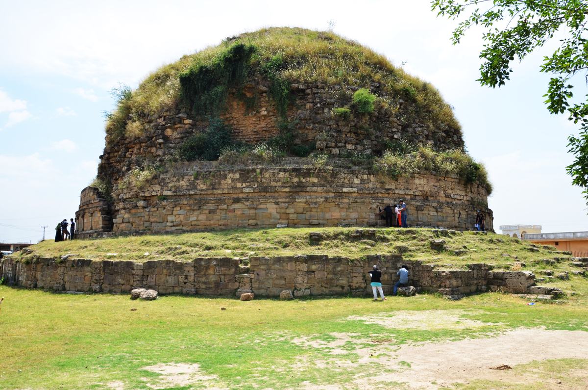 Mankiala Stupa, a large grassy stone dome with visitors at its base