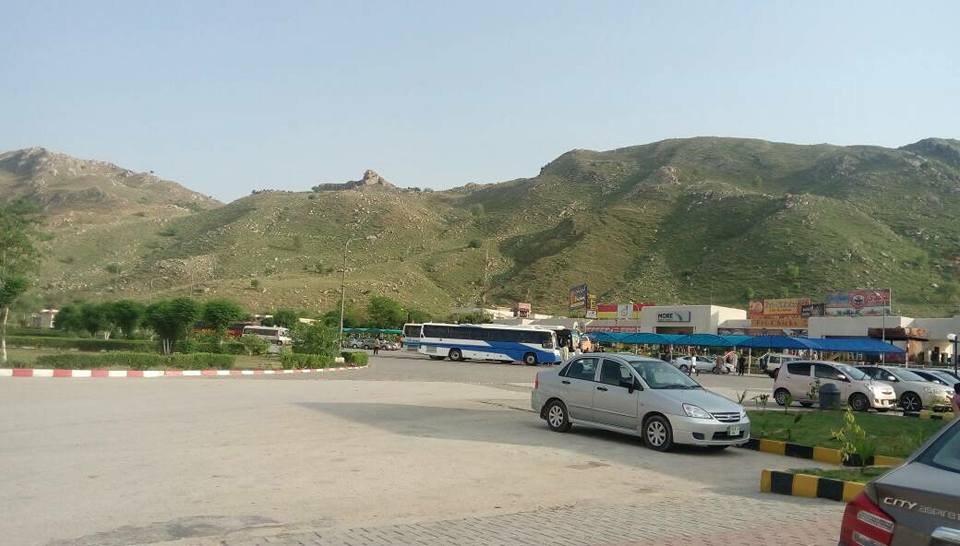 Car park and buses at the Kallar Kahar rest area on the M-2 motorway with green Salt Range hills behind