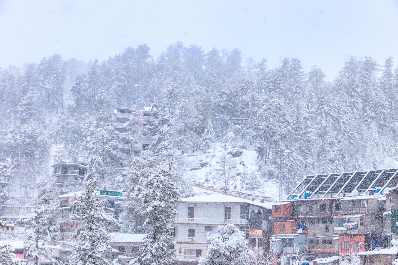 Snow falling over pine forests and hillside houses in Murree, a day trip from LEORK Hotels Rawalpindi